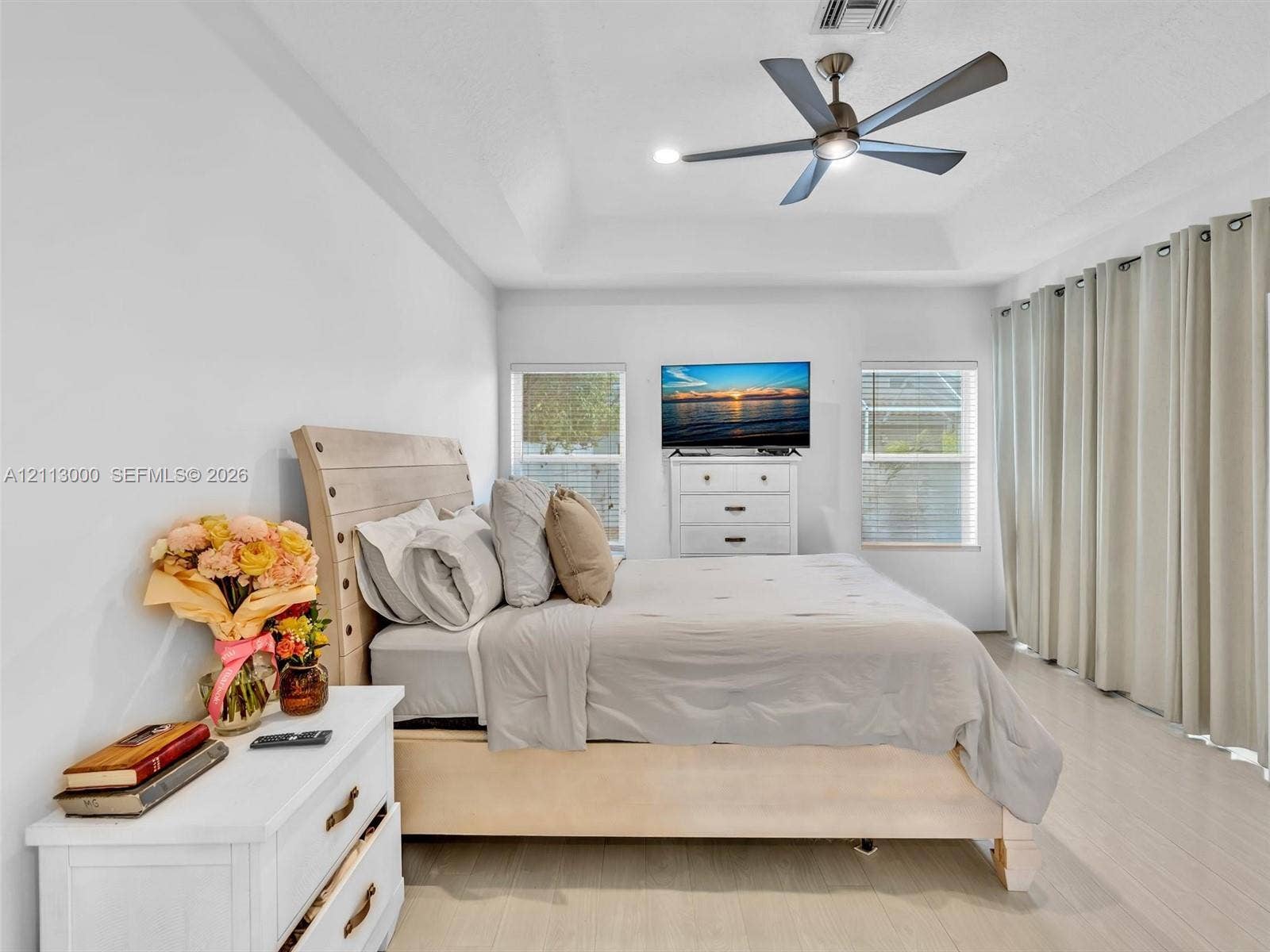 10860 La Salinas Circle, Boca Raton, FL 33428 Tray ceiling, multi-blade ceiling fan with integrated lighting, wood-finish flooring, and large windows with full-length window treatments