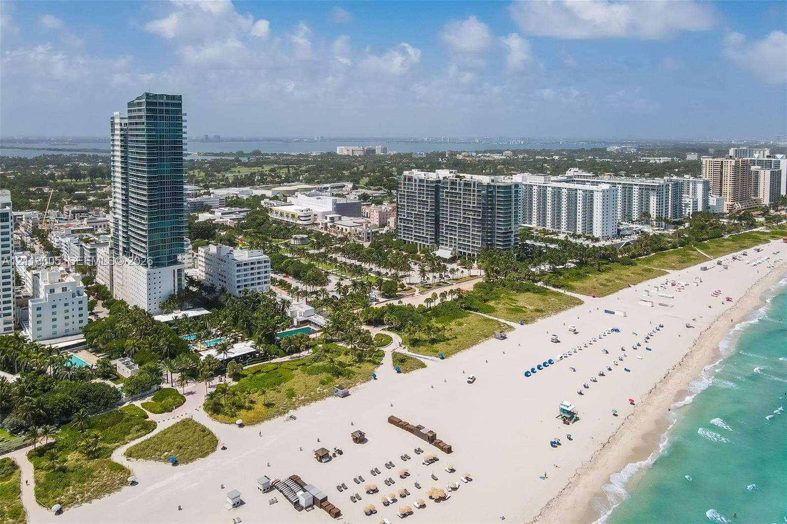 Aerial perspective of coastal high-rise development featuring direct oceanfront access, extensive white sand shoreline, and proximity to regional metropolitan infrastructure