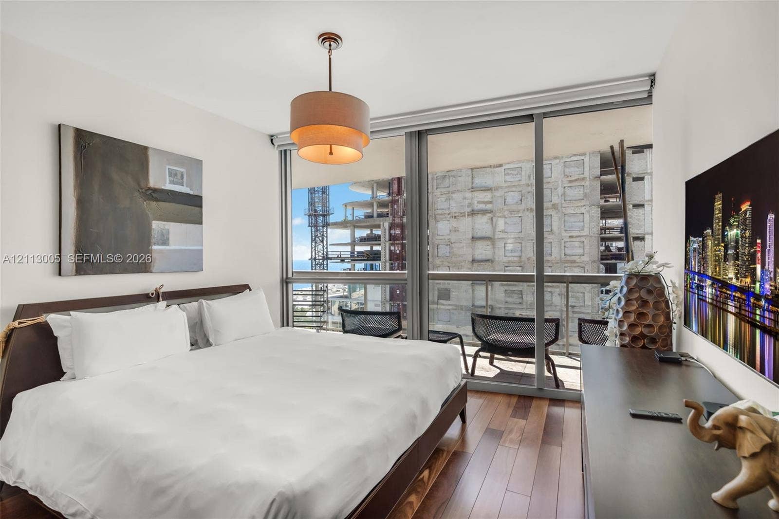 Floor-to-ceiling windows, wood-finish flooring, sliding glass door access to a private balcony, and a multi-tiered drum pendant light fixture