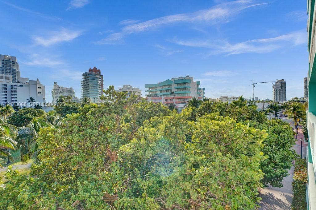 Exterior balcony featuring white metal railings and a cityscape backdrop with mature trees and palms