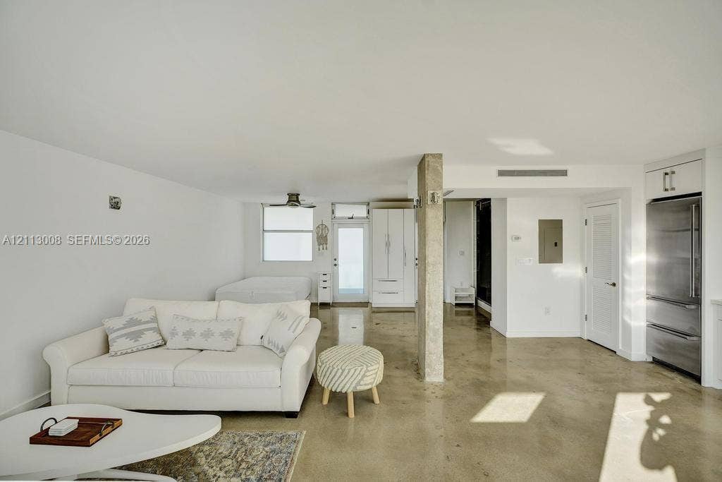 Polished concrete flooring, exposed concrete structural column, stainless steel refrigerator, and custom white cabinetry