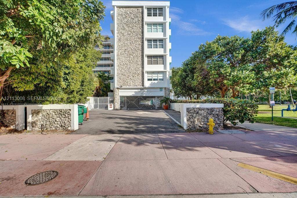 Mid-rise building featuring a textured stone facade, white structural framing, and a gated entrance