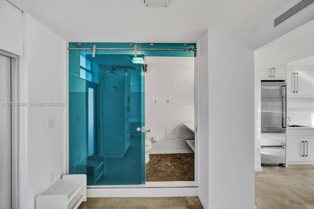 Sliding blue-tinted glass door featuring a stainless steel track system, white wall tiling, stone-finish flooring, and built-in shelving