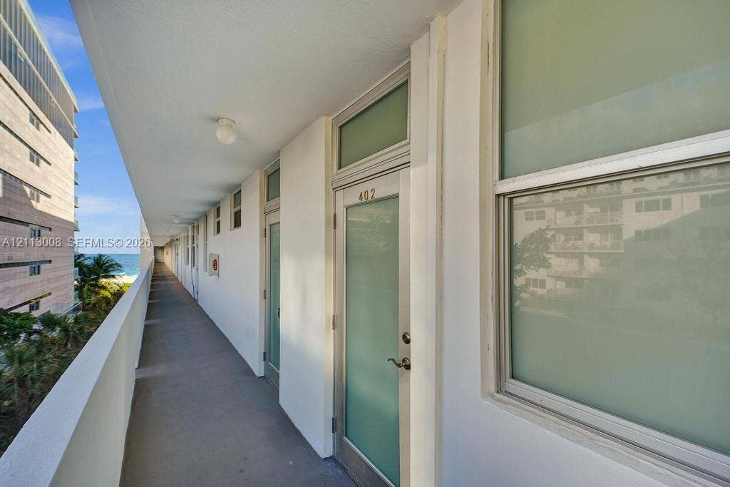 Covered exterior walkway featuring flush-mount lighting, glass-paneled entry doors with transom windows, and solid perimeter railings