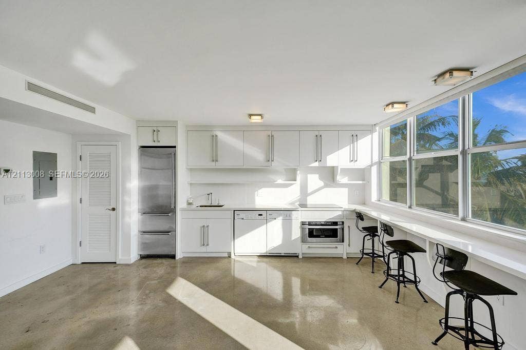 Kitchen featuring white cabinetry, stainless steel appliances, polished concrete flooring, a long built-in window counter, and expansive windows