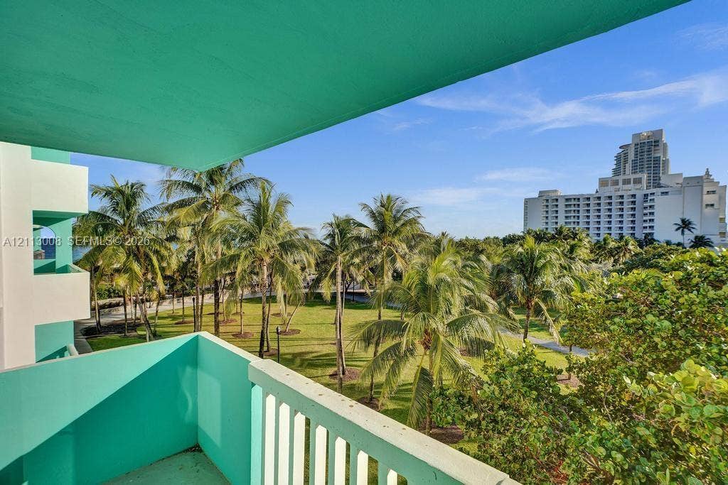 Private balcony with turquoise concrete railing overlooking a landscaped park with mature palm trees