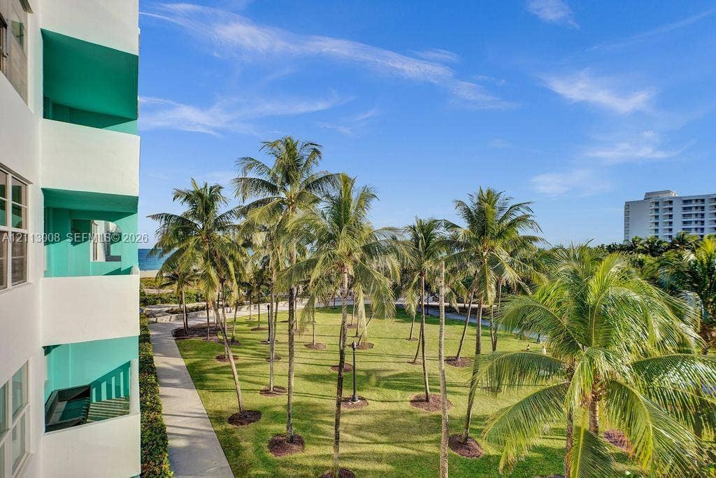 Multi-story exterior with private balconies featuring teal-accented walls, overlooking an expansive grass courtyard with mature palm trees
