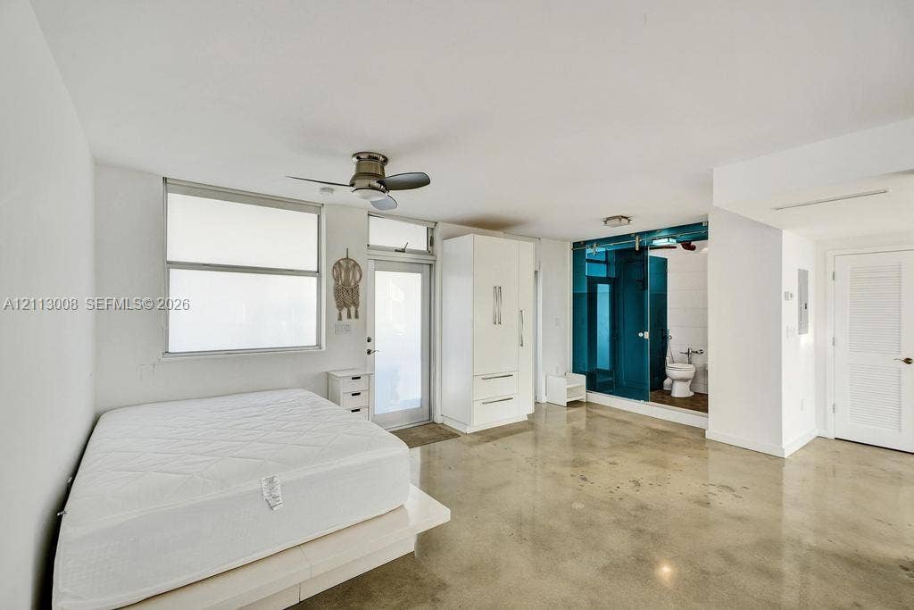 Polished concrete flooring, built-in white storage cabinetry, ceiling fan, and sliding glass bathroom door with teal-tinted finish