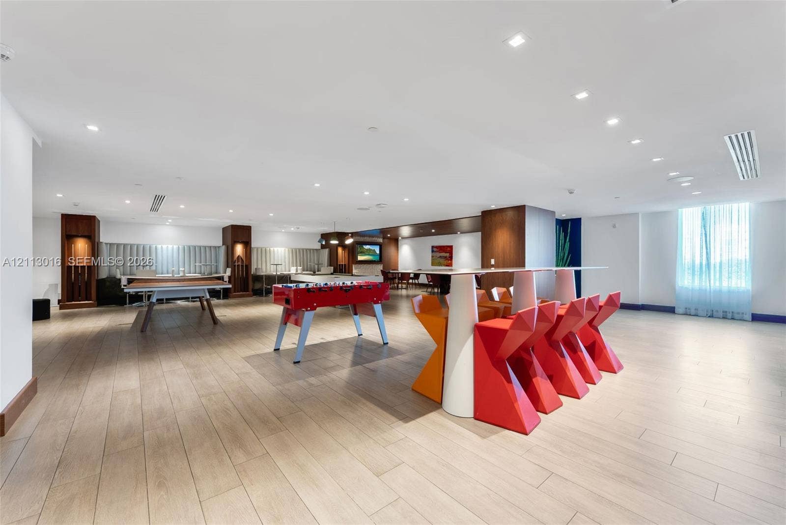 Expansive recreation area featuring wood-finish flooring, recessed lighting, built-in cabinetry, and floor-to-ceiling windows with window treatments