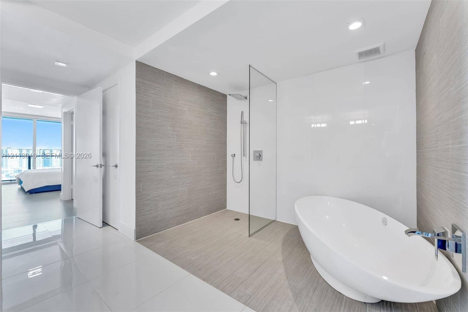 Freestanding soaking tub with a wall-mounted polished chrome faucet, walk-in shower with a glass enclosure, and textured grey wall tiling