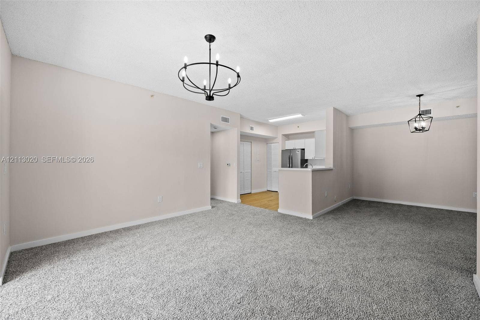 6968 SW 39th Street, #F104, Davie, Davie, FL 33314 Open-concept interior featuring neutral wall tones, wall-to-wall carpeting, and two black-finished geometric chandeliers