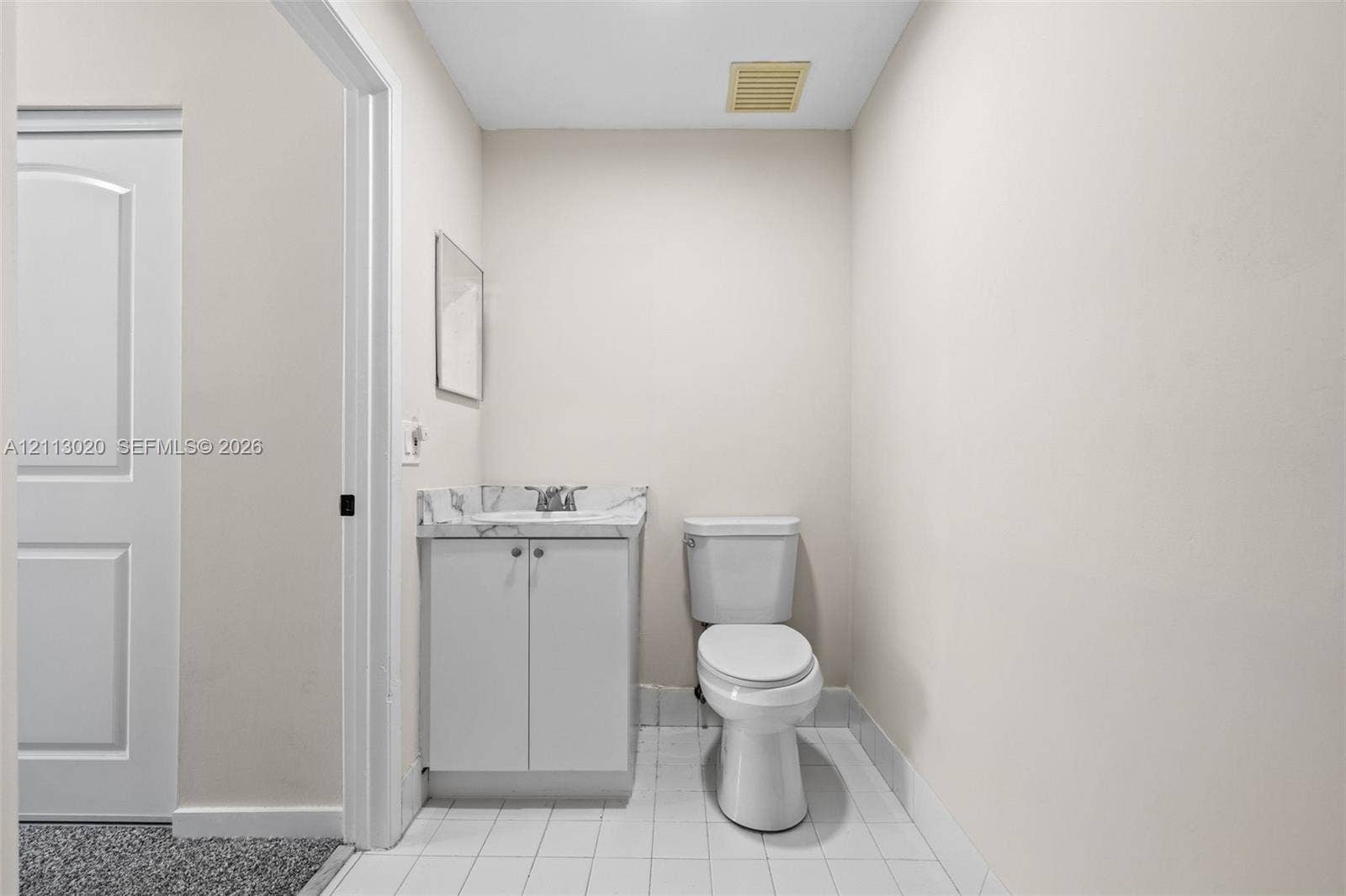 6968 SW 39th Street, #F104, Davie, Davie, FL 33314 Vanity featuring a stone-patterned countertop and undermount sink, white cabinetry, porcelain-style floor tiling, and a standard-height toilet