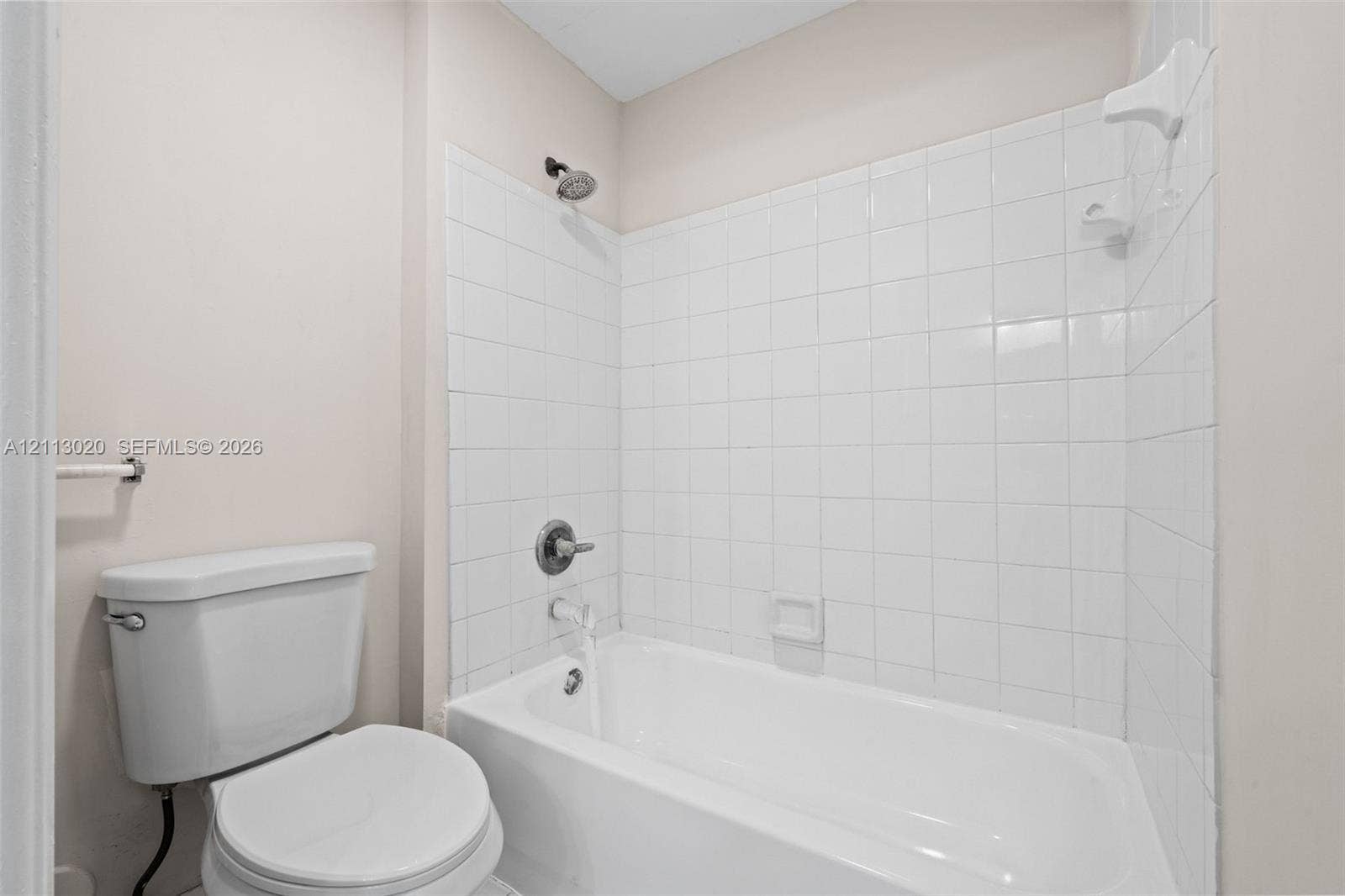 6968 SW 39th Street, #F104, Davie, Davie, FL 33314 Full-size bathtub with white tile surround, integrated soap dish, and wall-mounted shower fixture, paired with a standard-height porcelain toilet