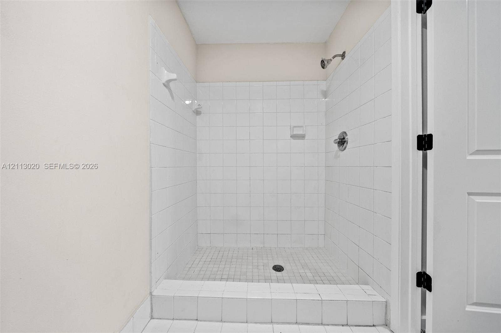 6968 SW 39th Street, #F104, Davie, Davie, FL 33314 Walk-in shower featuring white square-tile surround, tile-finished curb, integrated soap niche, wall-mounted shower head, and chrome fixtures