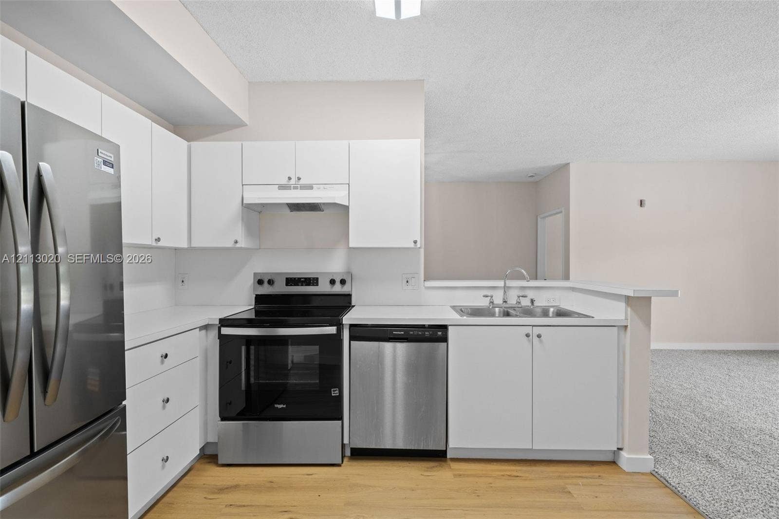 6968 SW 39th Street, #F104, Davie, Davie, FL 33314 Kitchen featuring white cabinetry, solid-surface countertops, stainless steel appliances, a double-basin sink, and wood-finish flooring