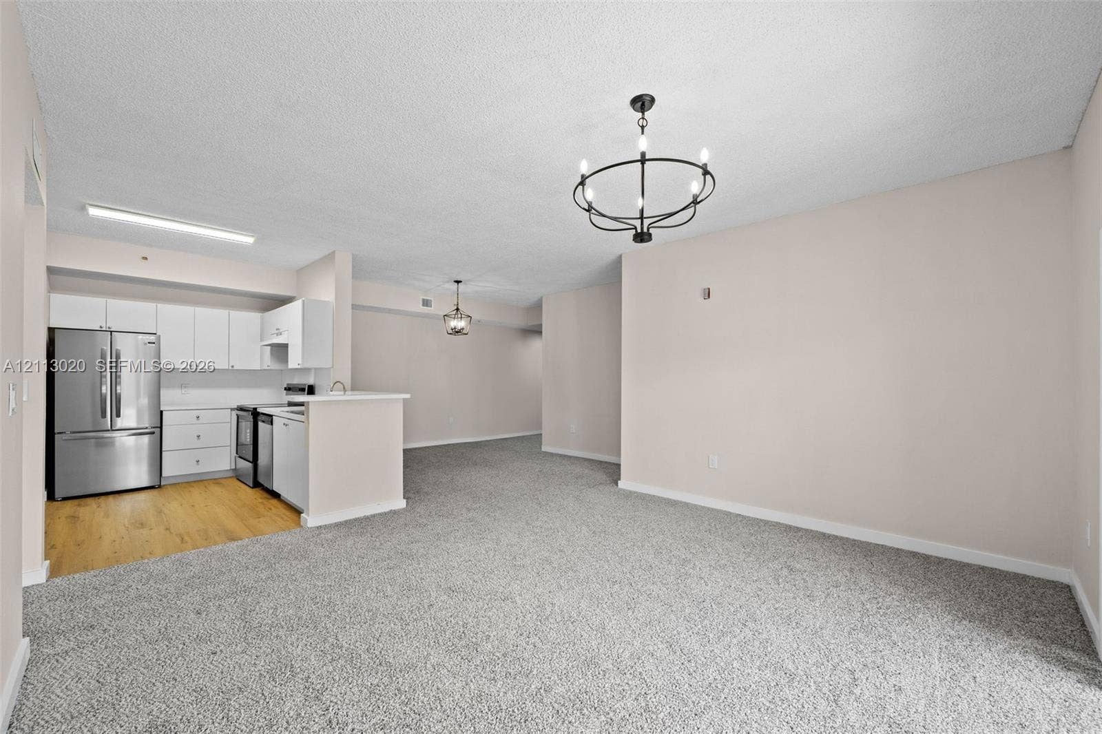 6968 SW 39th Street, #F104, Davie, Davie, FL 33314 Kitchen featuring white cabinetry, stainless steel refrigerator, and wood-finish flooring, complemented by a matte black circular chandelier and neutral carpeting