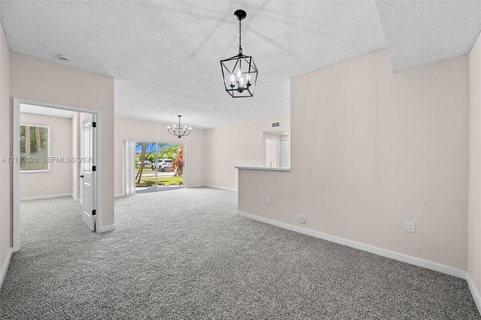 6968 SW 39th Street, #F104, Davie, Davie, FL 33314 Interior space featuring neutral-toned carpeting, geometric metal chandeliers, glass sliding doors, and a partial partition wall