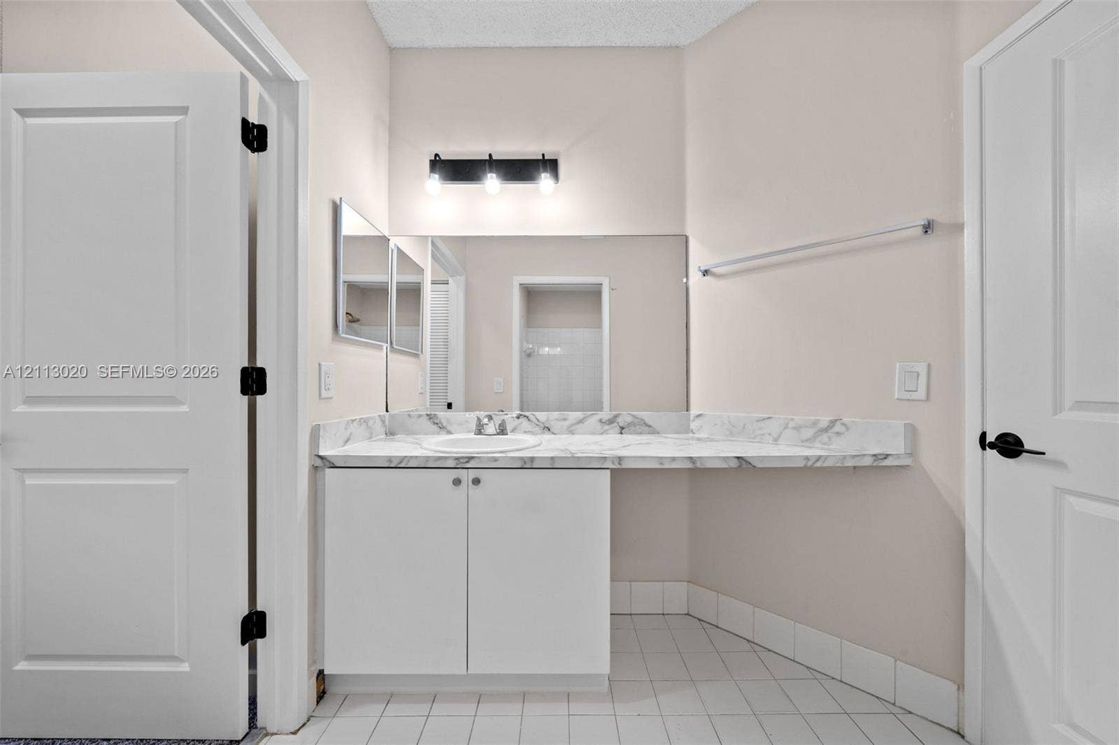 6968 SW 39th Street, #F104, Davie, Davie, FL 33314 Bathroom vanity featuring stone-patterned countertop with integrated sink, white cabinetry, wall-to-wall mirror, three-light fixture, and ceramic tile flooring
