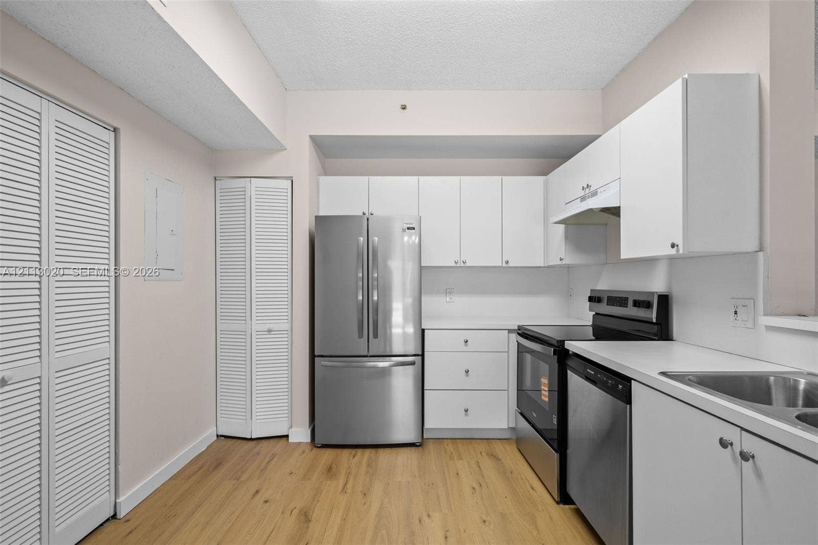 6968 SW 39th Street, #F104, Davie, Davie, FL 33314 Kitchen featuring white cabinetry, stainless steel appliances, solid-surface countertops, wood-finish flooring, and louvered-style closet doors