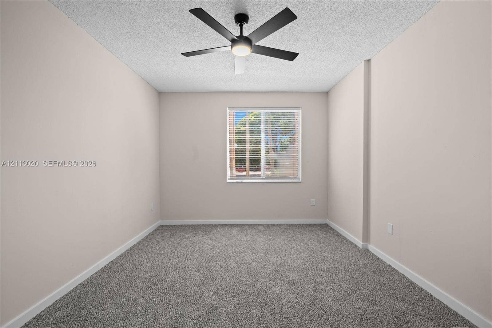 6968 SW 39th Street, #F104, Davie, Davie, FL 33314 Neutral-toned interior space featuring neutral wall-to-wall carpeting, a centered matte black ceiling fan with integrated lighting, and a single window with horizontal blinds