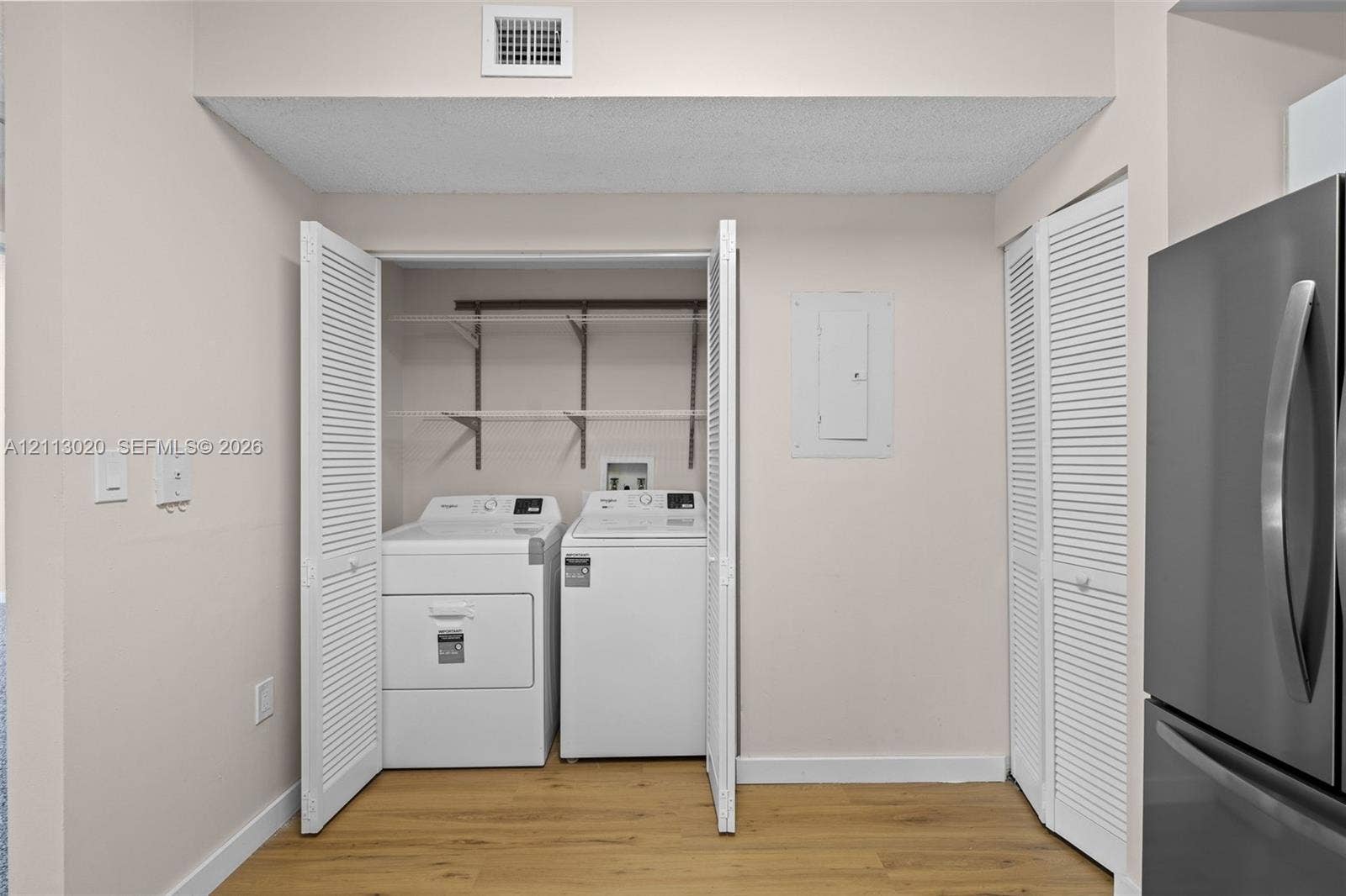 6968 SW 39th Street, #F104, Davie, Davie, FL 33314 Laundry area featuring white bi-fold louvered closet doors, adjustable wire shelving, and wood-finish flooring