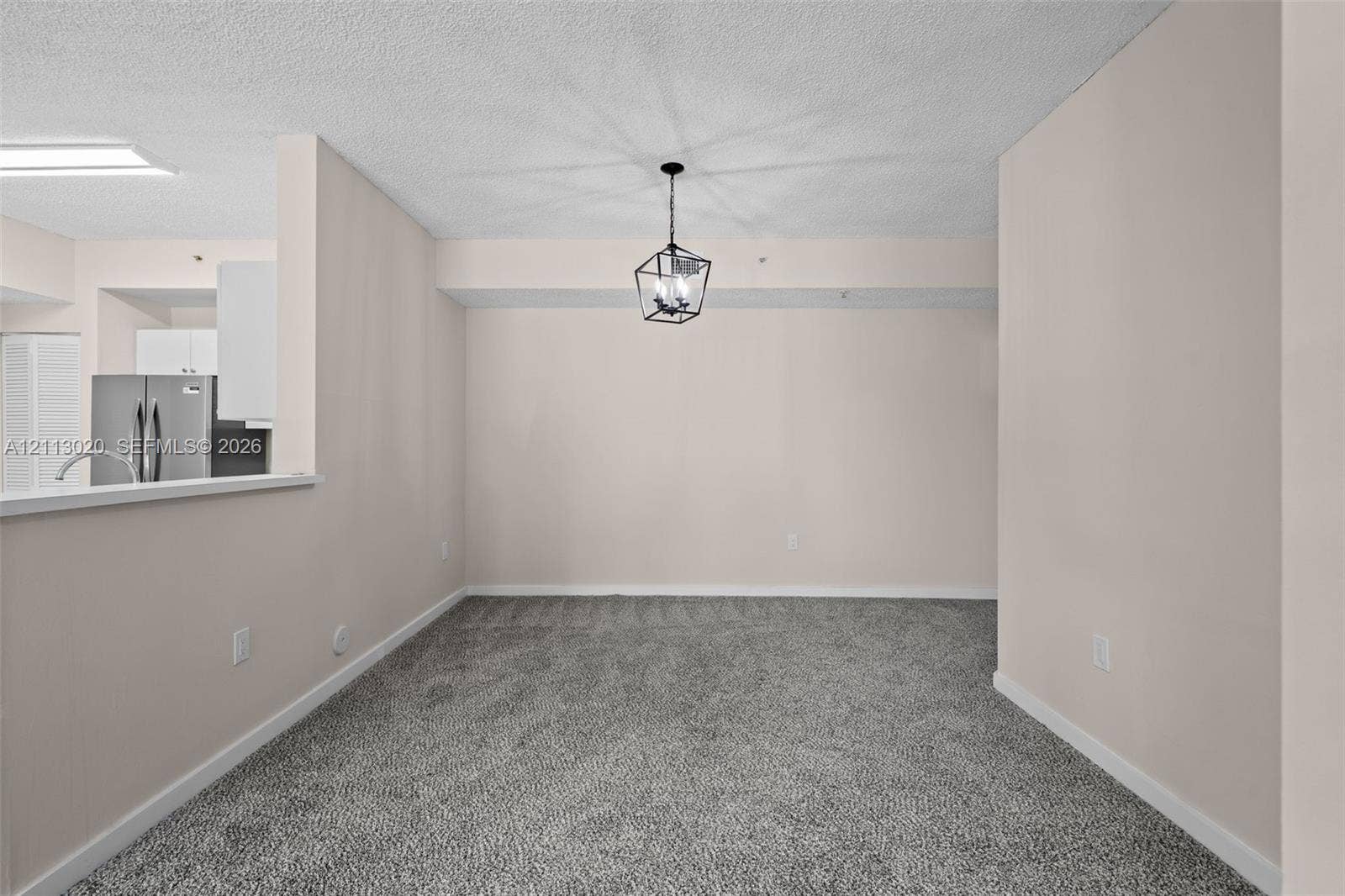 6968 SW 39th Street, #F104, Davie, Davie, FL 33314 Interior space featuring neutral wall tones, textured ceiling, wall-to-wall carpeting, and a geometric metal pendant light fixture