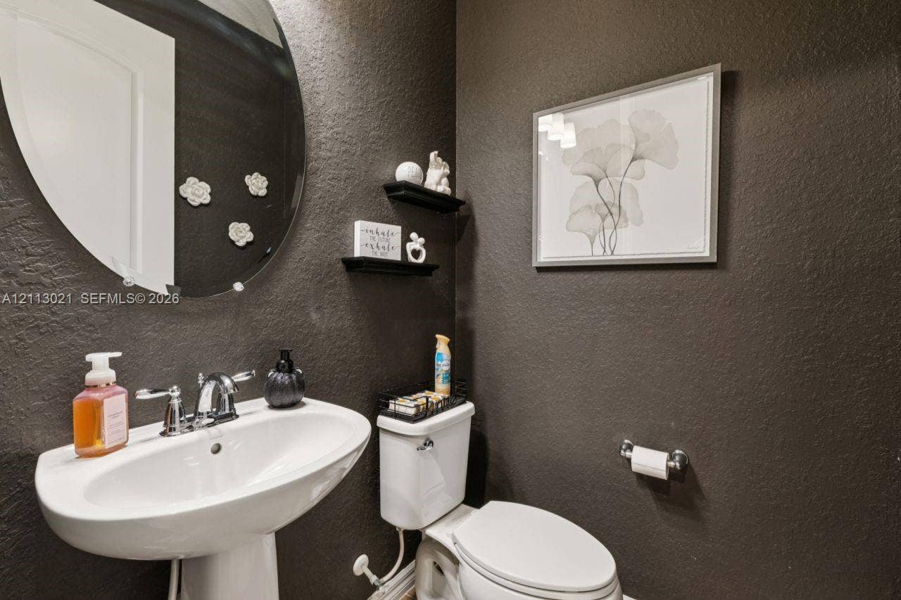 8228 Tailshot Court, Lake Worth, Lake Worth, FL 33467 Oval wall-mounted mirror, white ceramic pedestal sink, chrome finish faucet, two built-in floating shelves, and textured dark-toned walls