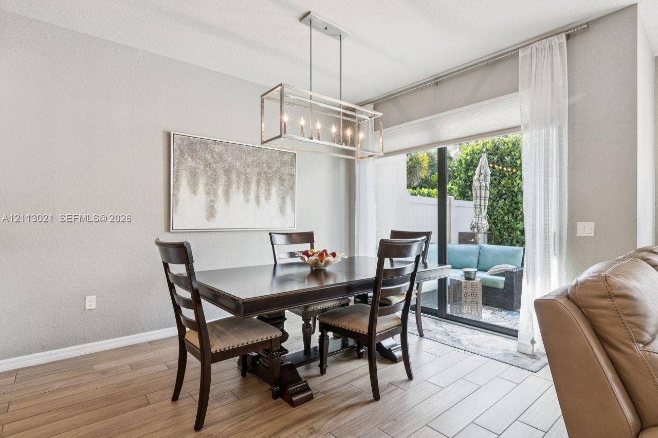 8228 Tailshot Court, Lake Worth, Lake Worth, FL 33467 Dining area featuring wood-finish tile flooring, a rectangular metal-frame chandelier, and sliding glass doors leading to a paved patio