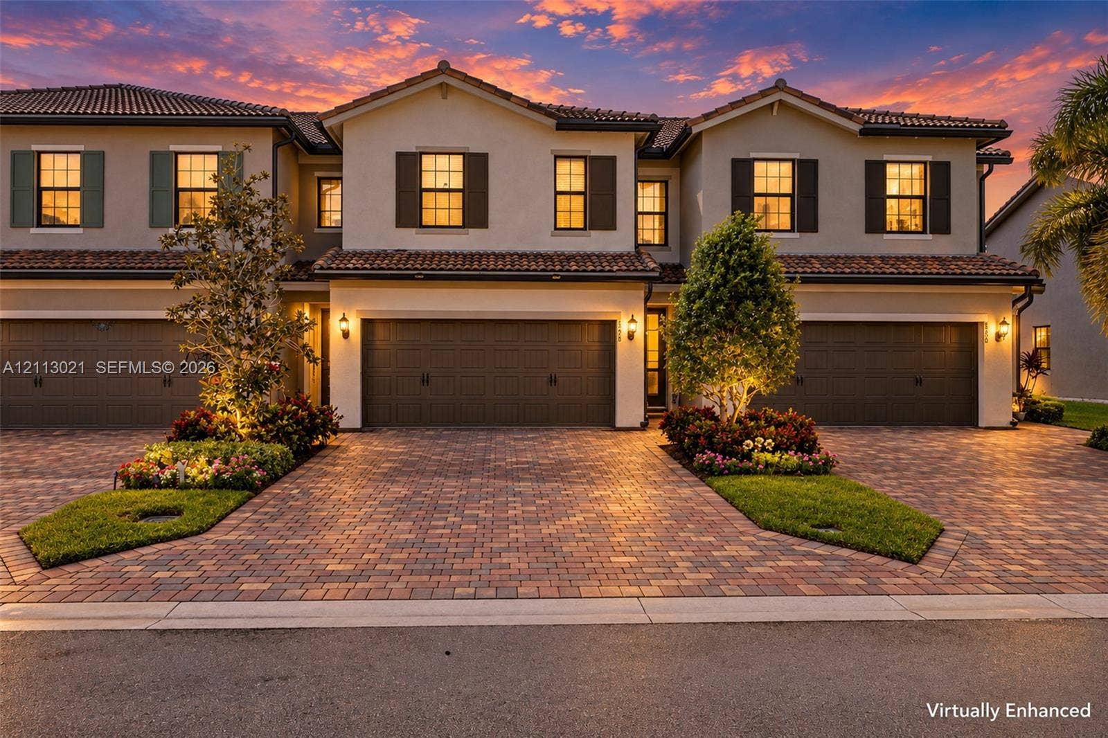 8228 Tailshot Court, Lake Worth, Lake Worth, FL 33467 Stucco exterior featuring a clay tile roof, multi-car garages, and a paved brick driveway with curated landscaping