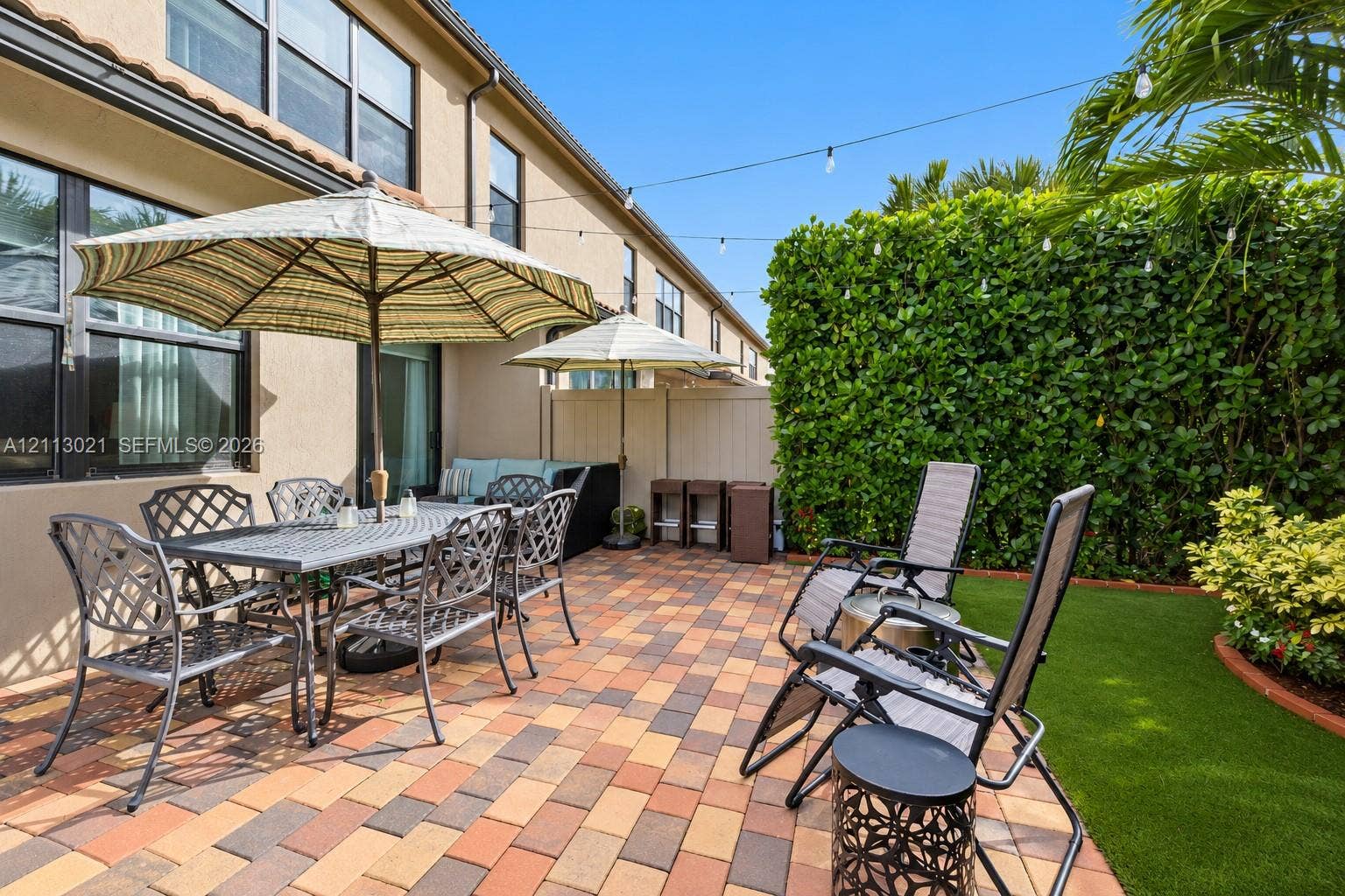 8228 Tailshot Court, Lake Worth, Lake Worth, FL 33467 Paver patio featuring integrated string lighting, synthetic turf lawn, and perimeter privacy hedges