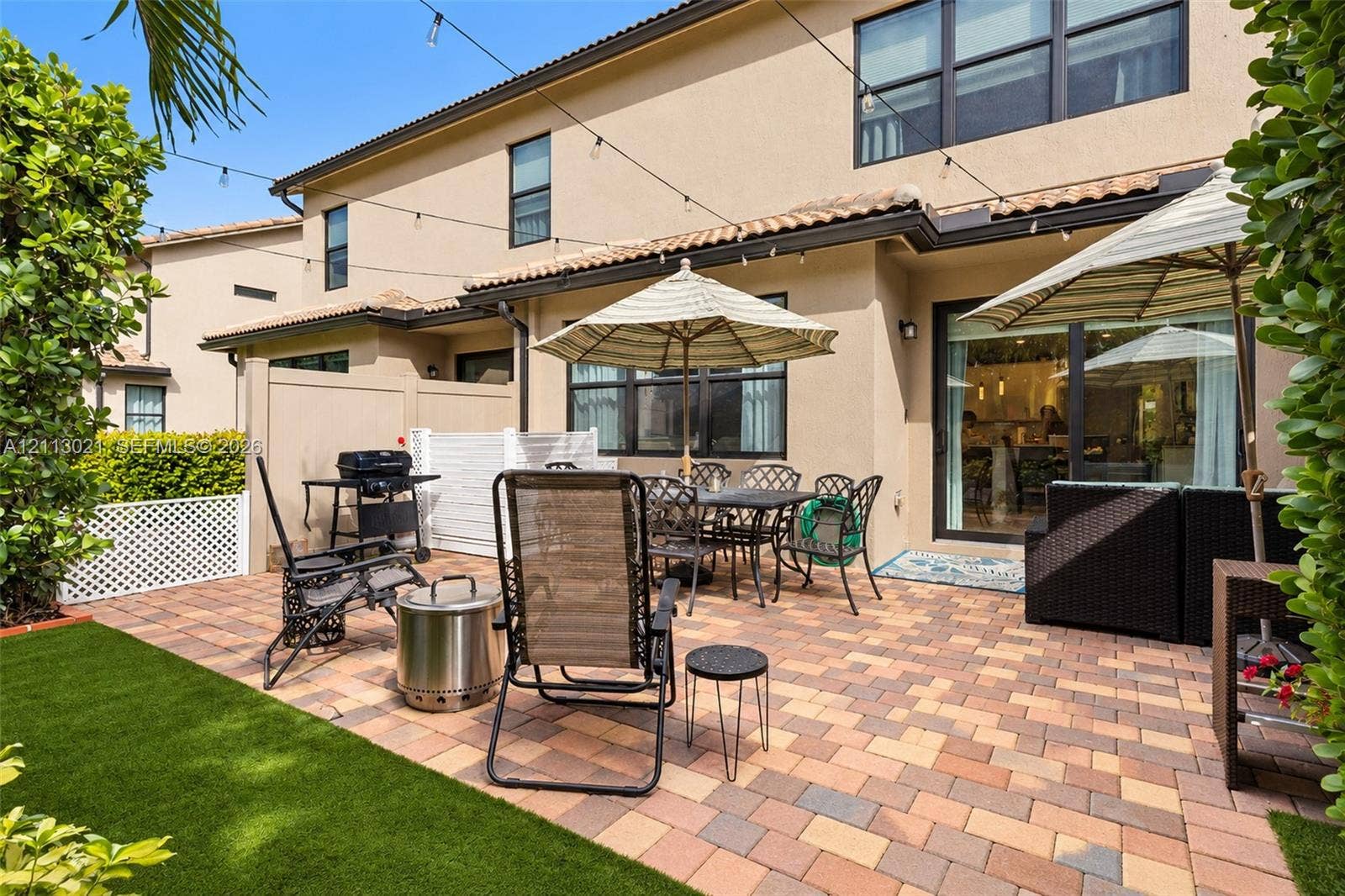 8228 Tailshot Court, Lake Worth, Lake Worth, FL 33467 Rear exterior space featuring a paved stone patio, artificial turf lawn, privacy fencing with lattice detailing, and overhead string lighting