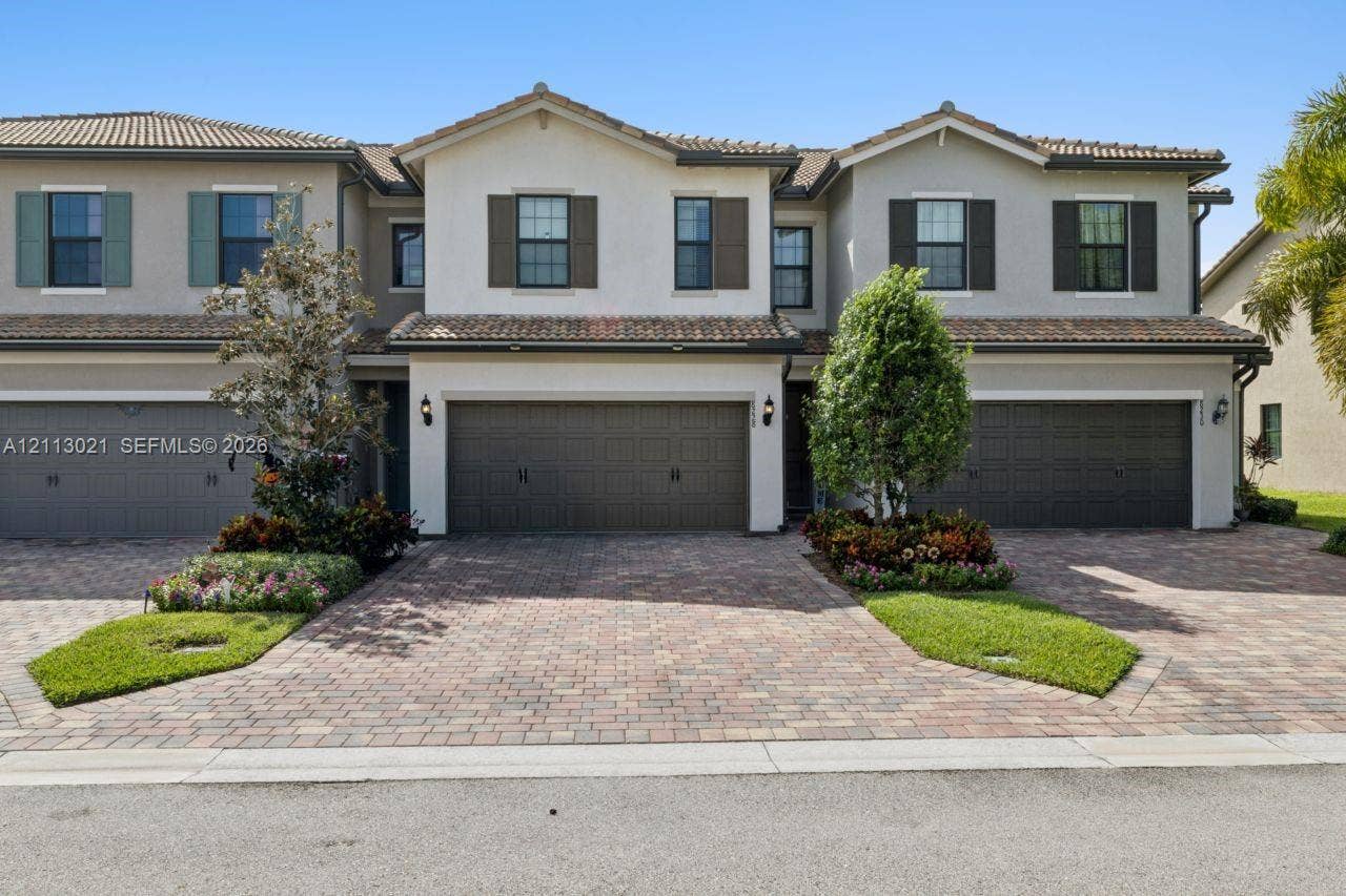 8228 Tailshot Court, Lake Worth, Lake Worth, FL 33467 Multi-story exterior featuring a neutral stucco facade, decorative shutters, tile roofing, and brick-paver driveways with integrated landscaping