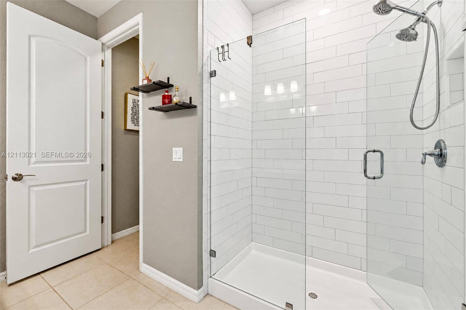 8228 Tailshot Court, Lake Worth, Lake Worth, FL 33467 Walk-in shower with white subway tile surround, frameless glass door, dual shower heads, and built-in recessed shelf, complemented by large-format tile flooring and a solid-core interior door
