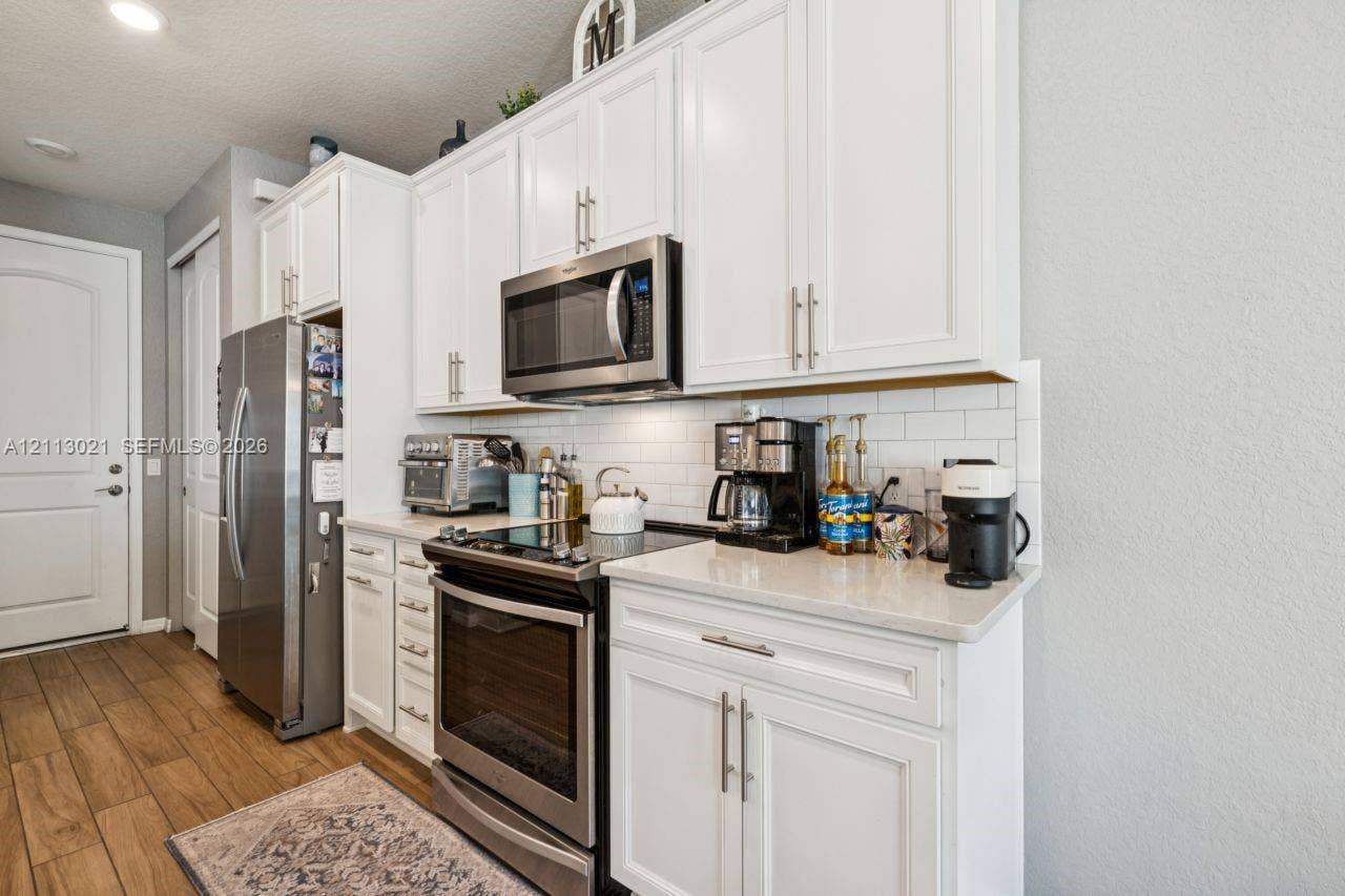 8228 Tailshot Court, Lake Worth, Lake Worth, FL 33467 Kitchen featuring white Shaker-style cabinetry, stainless steel appliances, quartz countertops, and a white subway tile backsplash, complemented by wood-finish flooring