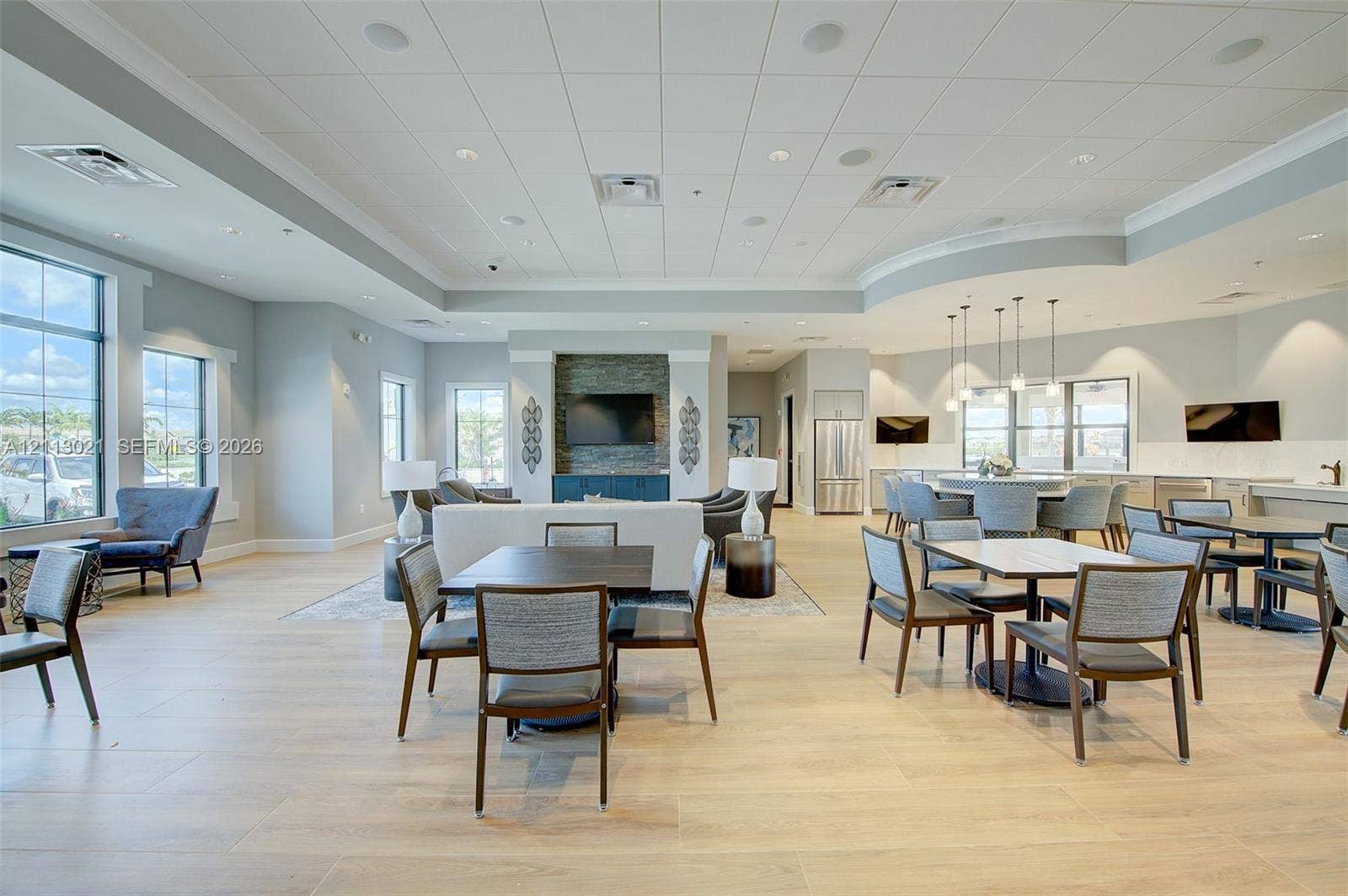 8228 Tailshot Court, Lake Worth, Lake Worth, FL 33467 Open-concept common area featuring wood-finish flooring, tray ceiling with recessed lighting, stone-accented wall with built-in media cabinet, and a kitchenette with stainless steel appliances