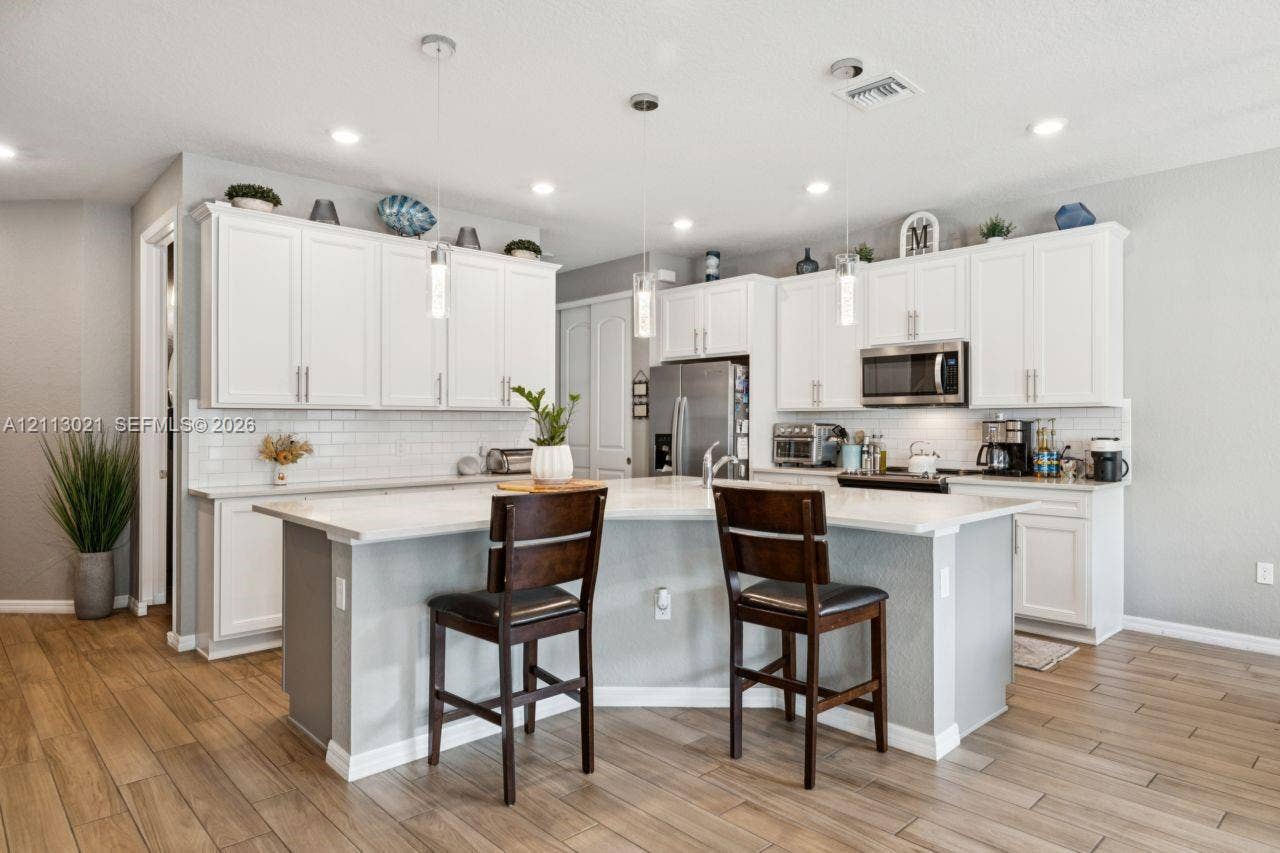 8228 Tailshot Court, Lake Worth, Lake Worth, FL 33467 Kitchen featuring white shaker-style cabinetry, a central island with a solid-surface countertop, white subway tile backsplash, stainless steel appliances, and wood-finish flooring
