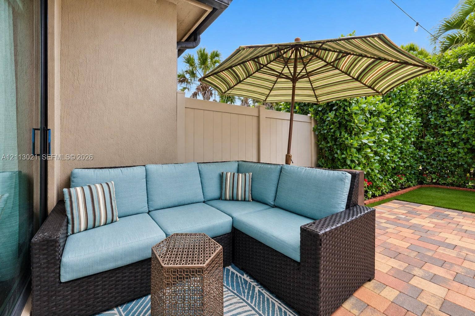 8228 Tailshot Court, Lake Worth, Lake Worth, FL 33467 Private outdoor patio featuring multi-tone paver flooring, synthetic turf, and a solid perimeter privacy fence with mature shrubbery