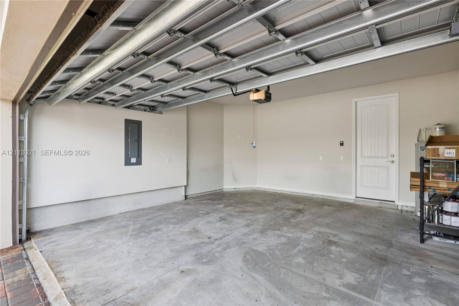 8228 Tailshot Court, Lake Worth, Lake Worth, FL 33467 Finished garage featuring concrete flooring, a panel door, exposed ceiling joists, and an electrical service panel