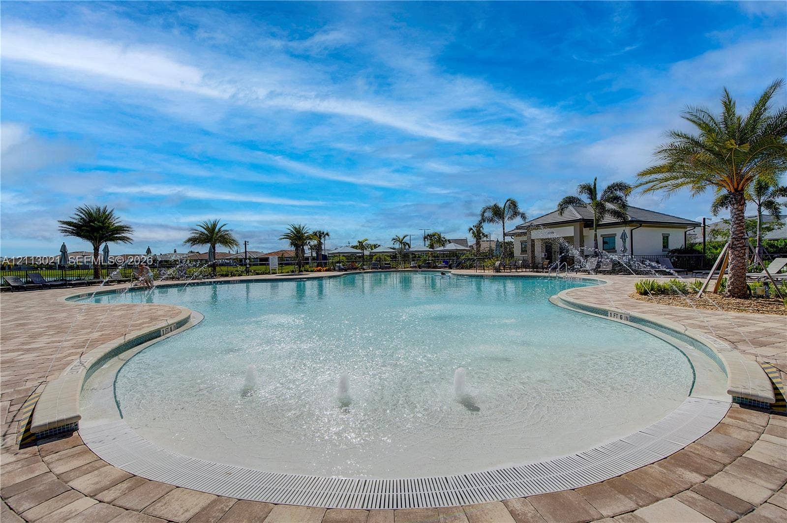 8228 Tailshot Court, Lake Worth, Lake Worth, FL 33467 Swimming pool featuring a beach-entry slope, integrated water fountain jets, and paver stone hardscaping surrounded by mature palm trees