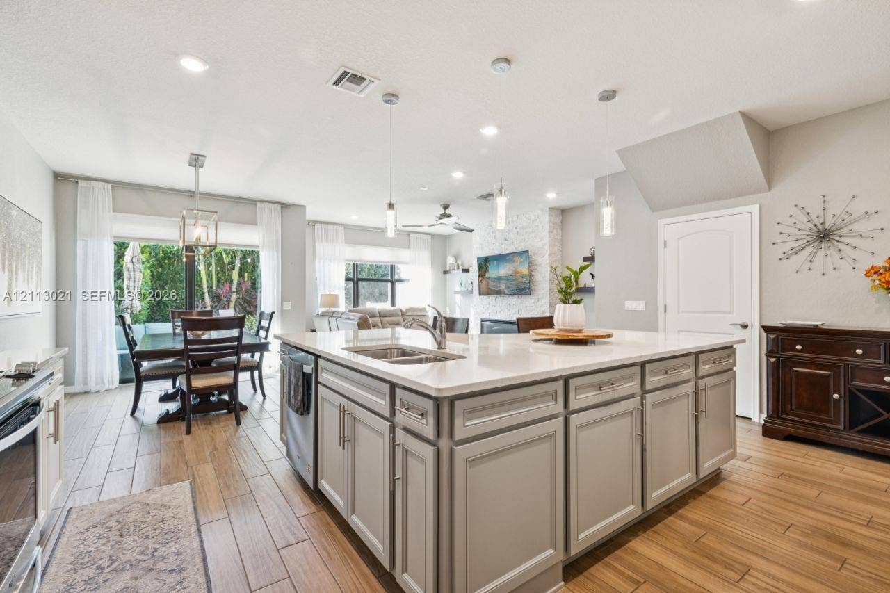 8228 Tailshot Court, Lake Worth, Lake Worth, FL 33467 Kitchen featuring a large central island with light-toned cabinetry, solid surface countertops, a stainless steel double-basin undermount sink, pendant lighting, and wood-finish flooring