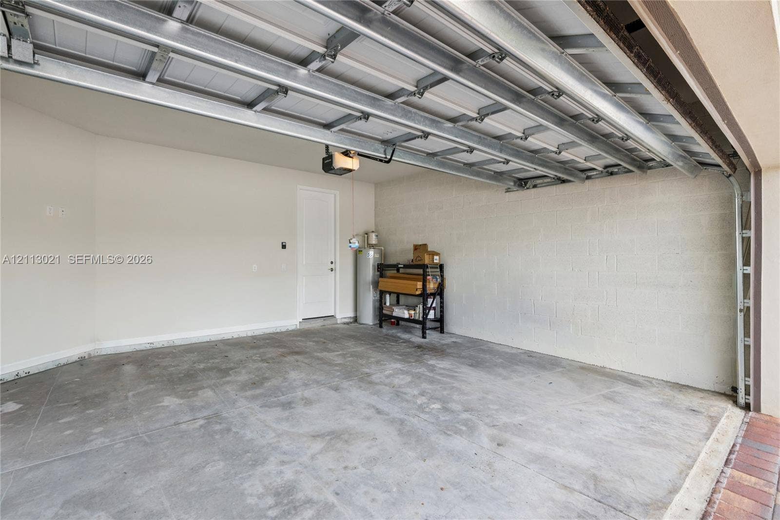8228 Tailshot Court, Lake Worth, Lake Worth, FL 33467 Two-car garage featuring finished concrete flooring, masonry block walls, an automatic overhead door opener, and an integrated water heater