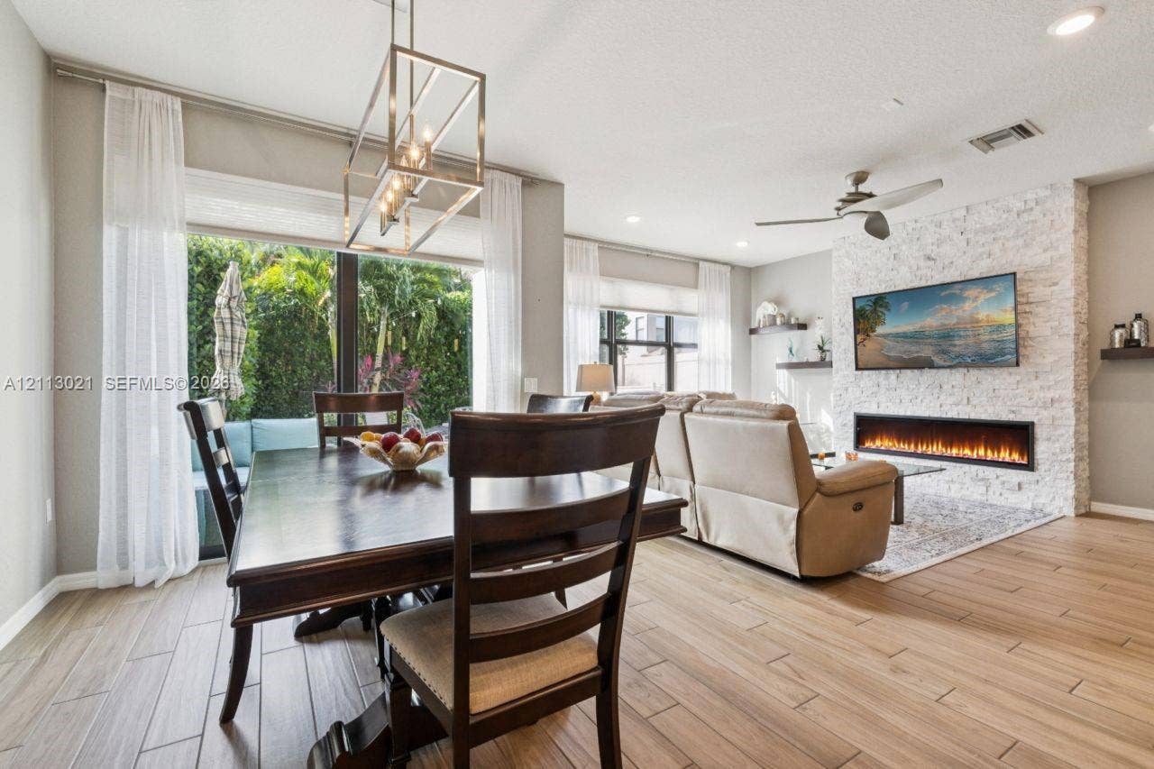 8228 Tailshot Court, Lake Worth, Lake Worth, FL 33467 Open-concept interior featuring wood-finish flooring, a textured stone accent wall with a linear electric fireplace, and a geometric metal pendant light