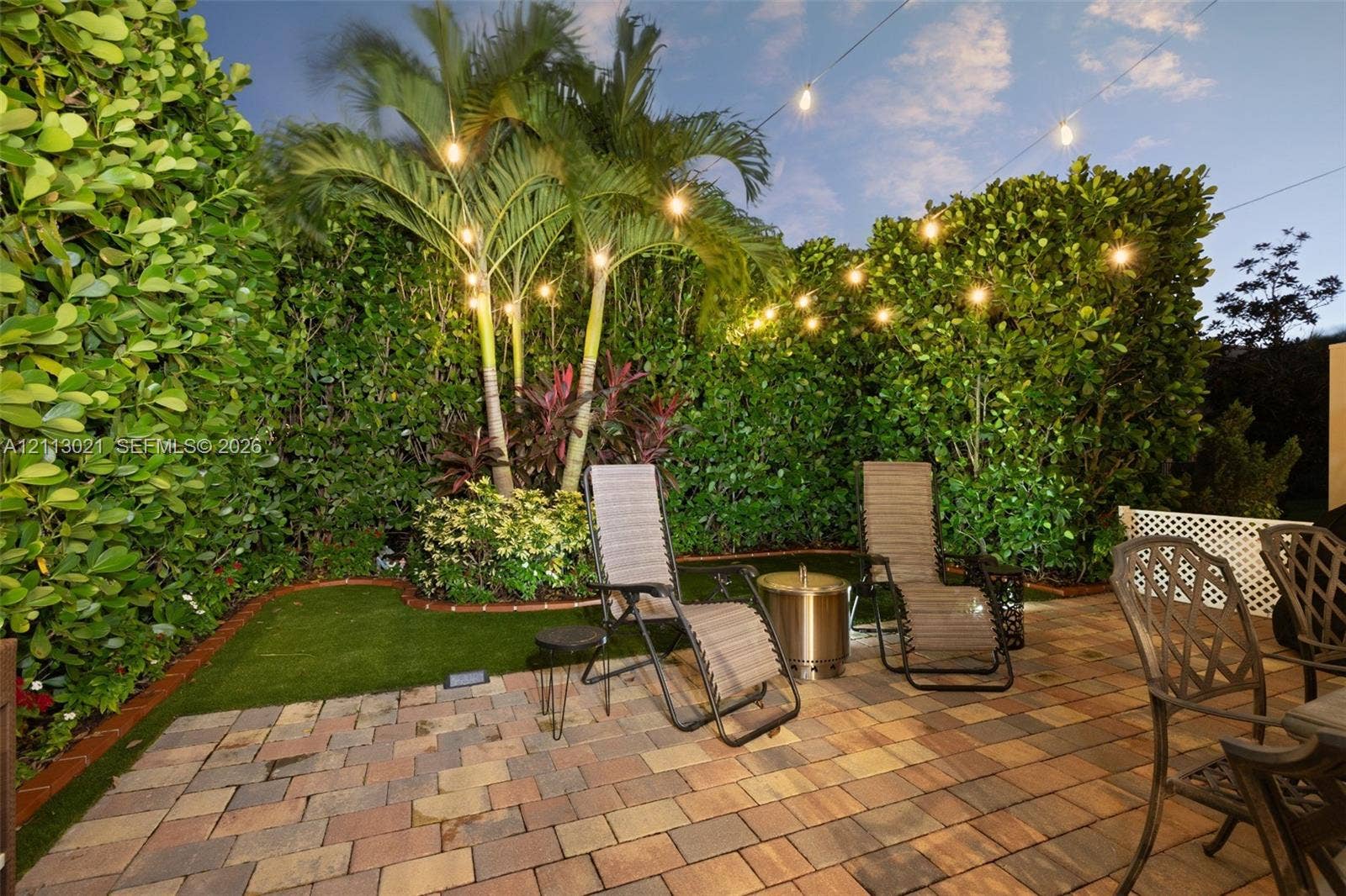 8228 Tailshot Court, Lake Worth, Lake Worth, FL 33467 Private outdoor space featuring a paved brick patio, manicured synthetic lawn, perimeter privacy hedges, and palm trees