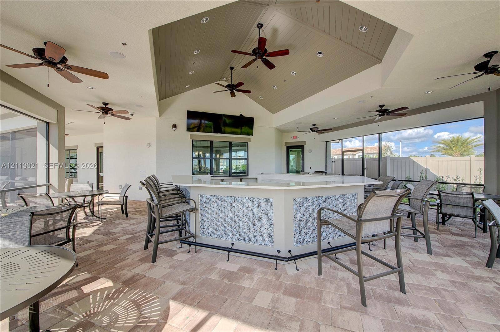 8228 Tailshot Court, Lake Worth, Lake Worth, FL 33467 Covered outdoor patio featuring a vaulted ceiling with tongue-and-groove detailing, custom built-in bar with stone-tiled facade, paver flooring, and multiple ceiling fans