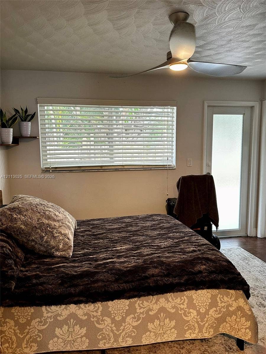 Textured ceiling, modern three-blade ceiling fan with integrated lighting, horizontal window blinds, and frosted glass exterior door
