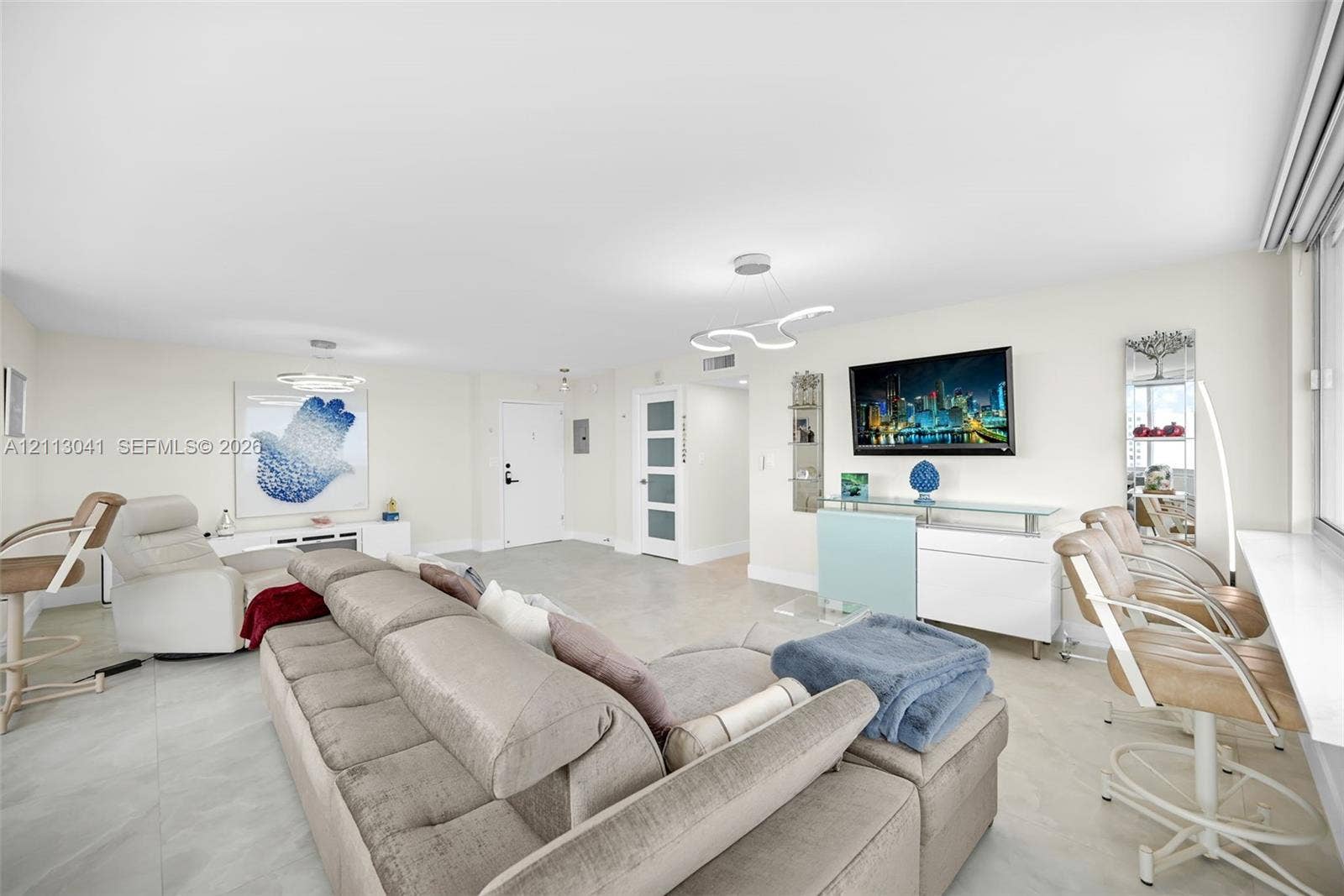 7135 Collins Avenue, #1426, Miami Beach, FL 33141 Open-concept living space featuring large-format tile flooring, recessed lighting, modern sculptural light fixtures, and a glass-paneled interior door