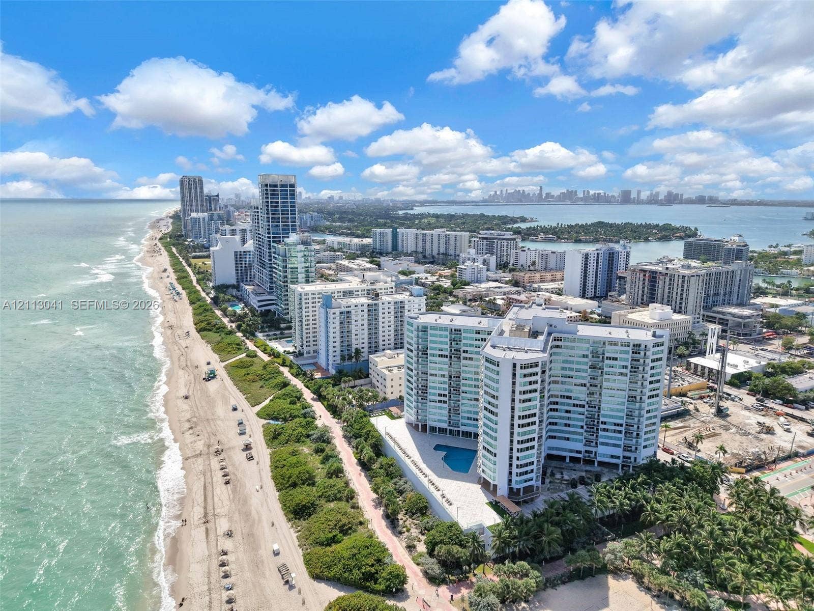 7135 Collins Avenue, #1426, Miami Beach, FL 33141 Aerial coastal perspective featuring a multi-story residential building with an attached ground-level swimming pool, situated on a beachfront parcel with direct shoreline access and surrounding palm landscaping