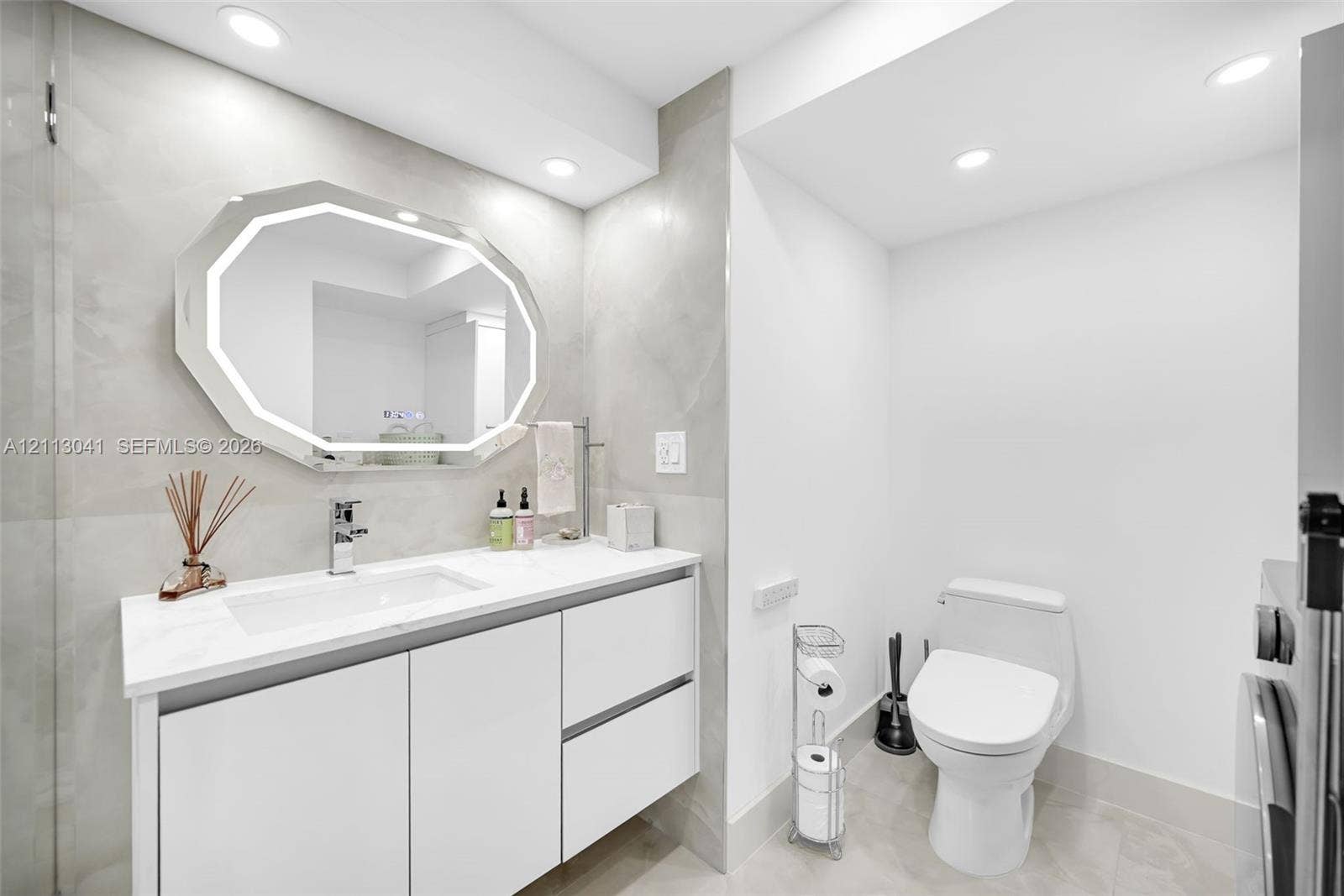7135 Collins Avenue, #1426, Miami Beach, FL 33141 Modern floating vanity featuring white cabinetry, a rectangular sink, and a light-toned countertop, paired with an octagonal LED-backlit mirror and large-format wall tile