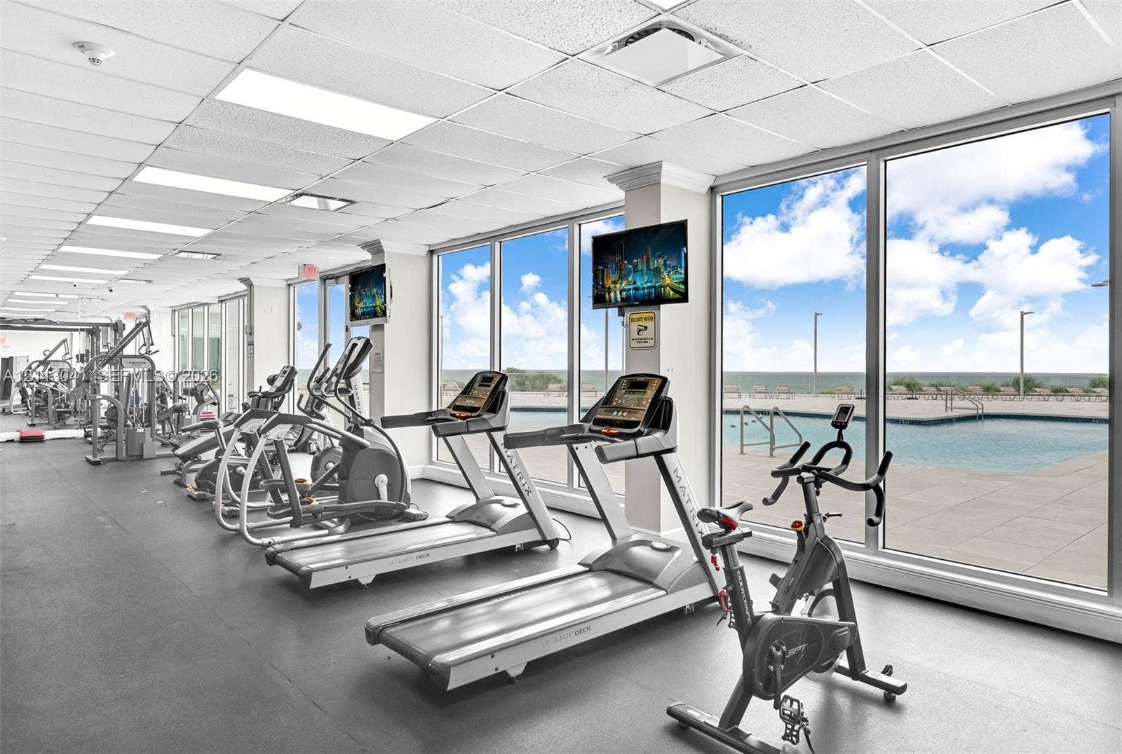 7135 Collins Avenue, #1426, Miami Beach, FL 33141 Fitness center featuring wall-to-wall windows, expansive natural light, rubber flooring, drop ceiling panels, and direct sightlines to an outdoor pool