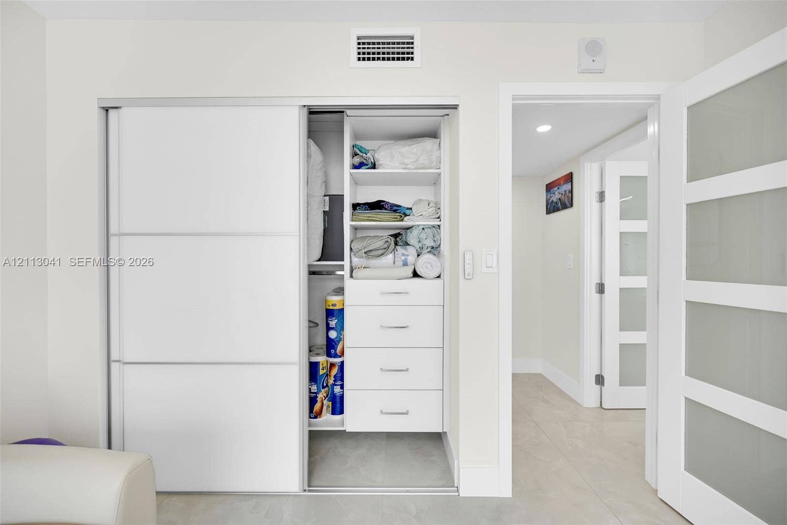 7135 Collins Avenue, #1426, Miami Beach, FL 33141 Storage closet featuring white sliding doors, built-in shelving, and integrated drawers, with paneled doors with frosted glass inserts